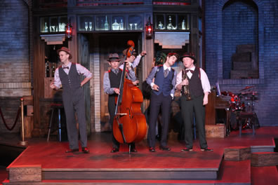 On the three-step platform of the speakeasy set, the musicians in vests and bowties sing, Dull with his standup bass, Costard holding his trumpet