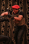 K.P. Powell as Hotspur in Henry IV, Part One, wearing a red cap, olive green and black t-shirt, and black pants weilding a sword