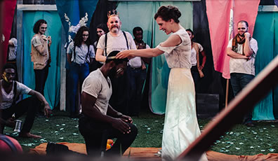Production photo of Thaisa crowning a kneeling Pericles with other castmembers around watching.
